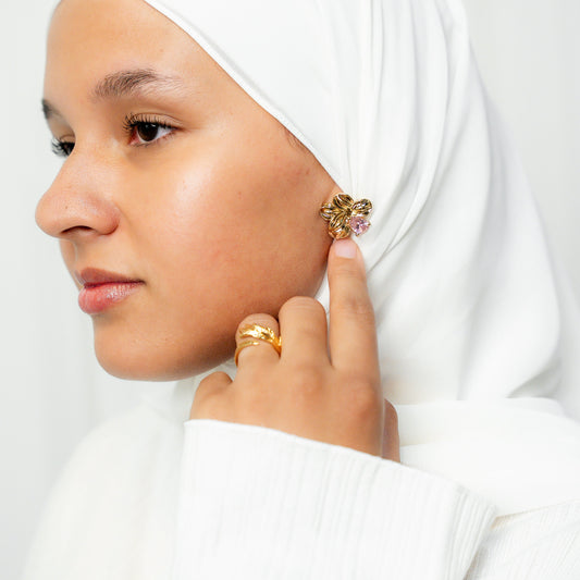 Woman wearing a white hijab and gold earrings against a plain background. harma gold plated earrings