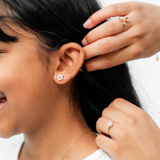 Person adjusting a child's earring with a white background. Harma Jewelry Gold Plated Little Bloom PINK Zirconia Earrings