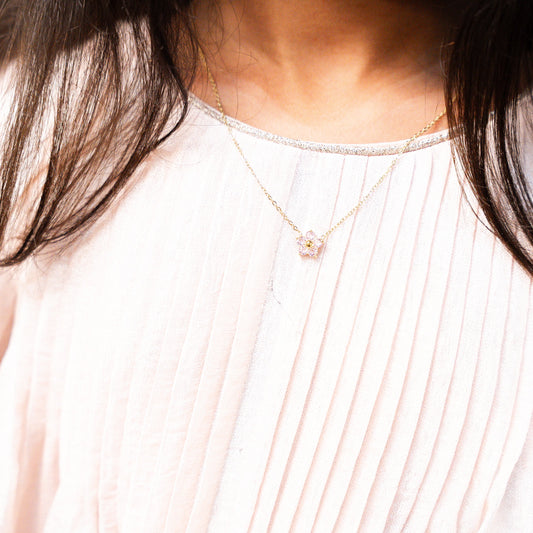 Close-up of a person wearing a white top with a necklace featuring a small pink pendant. Harma Jewelry Gold Plated Little Bloom PINK Zirconia Necklace