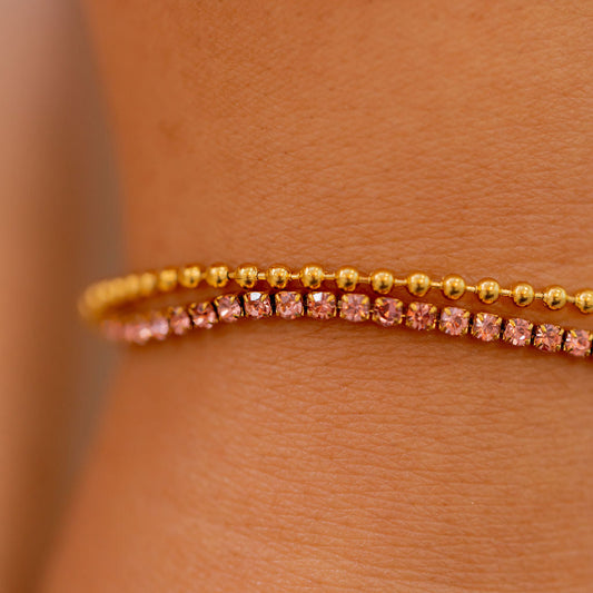 Close-up of a person wearing a gold bracelet with pink stones on a light brown background Harma Jewelry gold plated Dual Radiance PINK Tennis Bracelet
