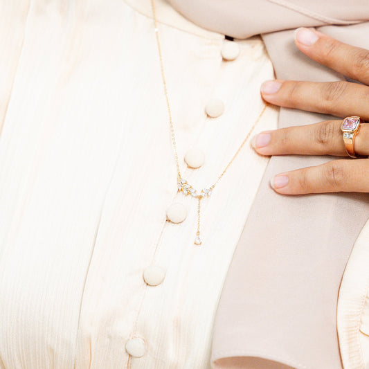 Close-up of a hand wearing an engagement ring on a light-colored garment. Harma Jewelry gold plated I Am Flourishing Sterling Silver Zirconia Necklace