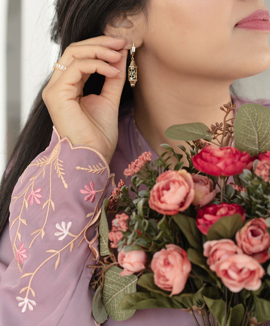 Person wearing a floral earring with a bouquet of pink roses. Harma Luminous Noor Lantern Necklace Set