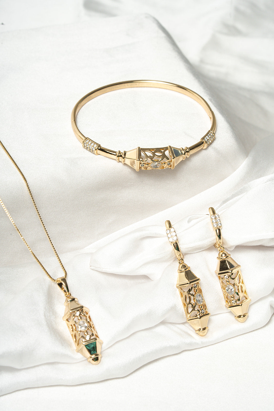 Gold jewelry set including necklace, earrings, and bracelet on a white fabric background Harma Luminous Noor Lantern Bracelet