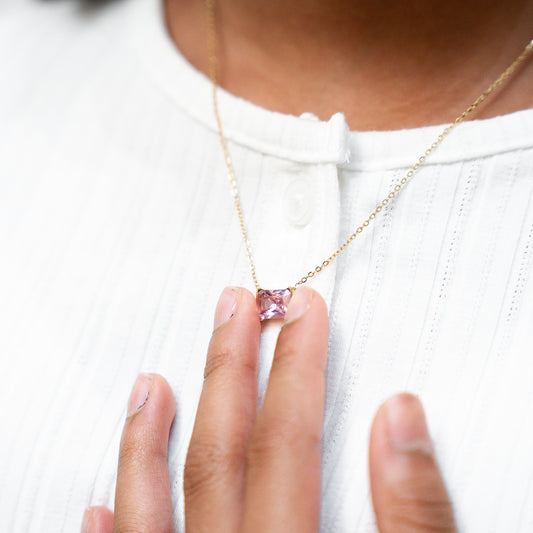 Person wearing a gold necklace with a pink pendant on a white background. Harma gold plated jewelry I Am Centered PINK Zirconia Necklace