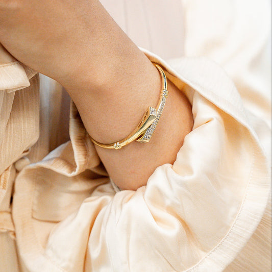 Close-up of a person wearing a beige dress with ruffled sleeves and a ring on a neutral background. Harma jewelry Gold plated I Am Whole Again Bangle Bracelet