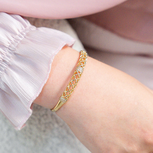 Close-up of a hand wearing gold jewelry with a soft pink background