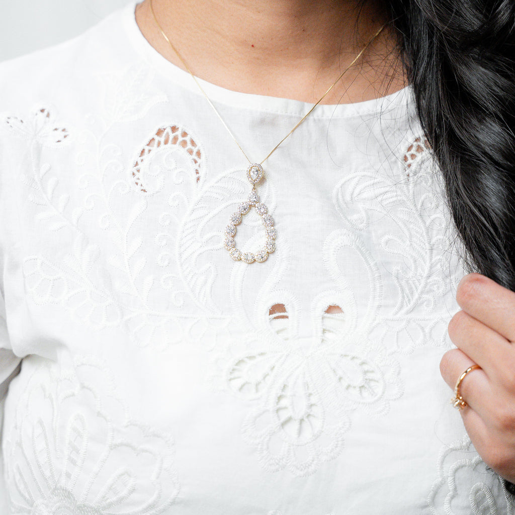Close-up of a person wearing a white embroidered top with a necklace and ring.