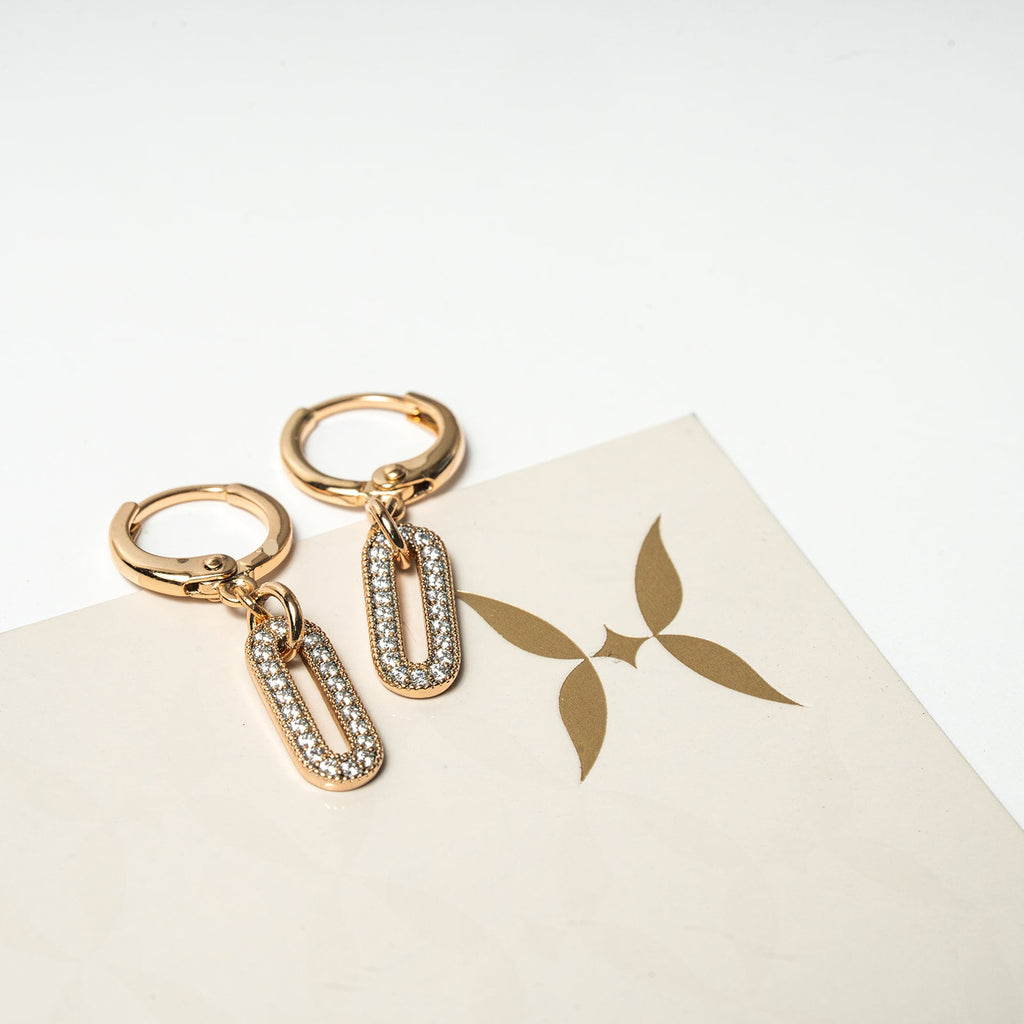 Gold hoop earrings with chain drops on a white surface with a brand logo.