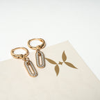 Gold hoop earrings with chain drops on a white surface with a brand logo.
