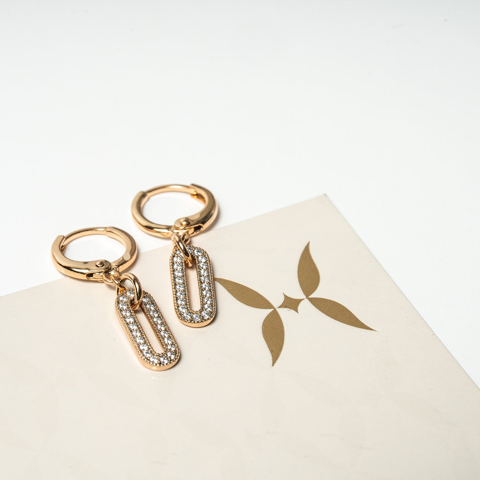 Gold hoop earrings with chain drops on a white surface with a brand logo.