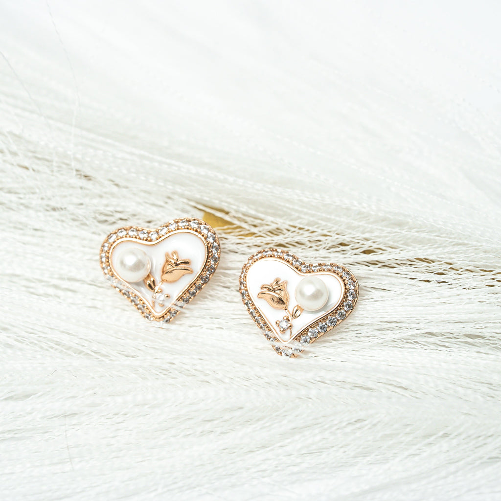 Heart-shaped earrings with pearl and gold details on a white fur background