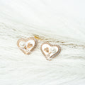 Heart-shaped earrings with pearl and gold details on a white fur background