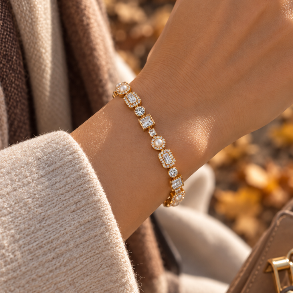 A close-up lifestyle shot of a gold bracelet with clear gemstones worn on a person's wrist, set against a soft-focus background of autumn leaves and a beige sweater. Autumn Constellation Zirconia Bracelet | Harma Jewelry 18k gold plated
