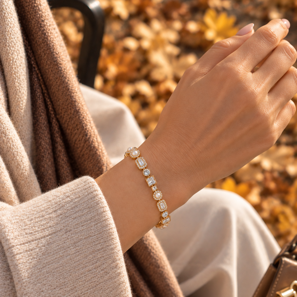 A gold bracelet with clear rectangular gemstones worn on a woman's wrist, shown in an outdoor setting with autumn leaves and a beige sweater. Autumn Constellation Zirconia Bracelet | Harma Jewelry 18k gold plated