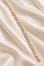 A gold tennis bracelet with clear gemstones and pearl accents, laid diagonally on a draped cream satin fabric background. Autumn Constellation Zirconia Bracelet | Harma Jewelry 18k gold plated