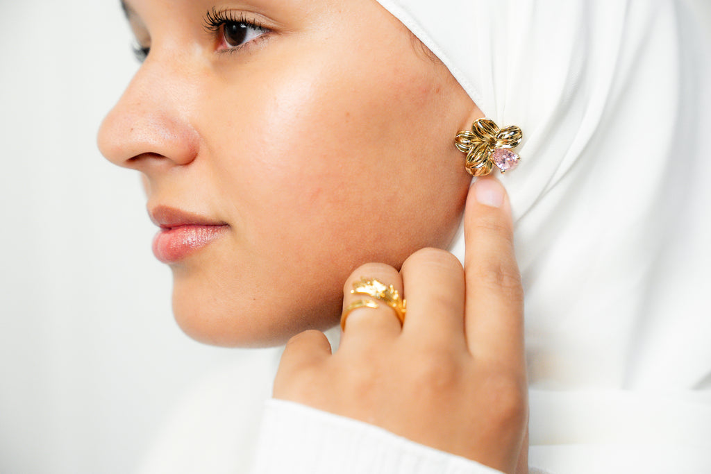 Woman wearing gold earrings and rings on a plain background