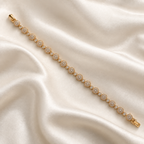 A gold tennis bracelet with pavé-set clear stones, arranged diagonally on a draped cream satin fabric background. Celestial Rhythm Zirconia Bracelet 18k gold plated harma jewelry