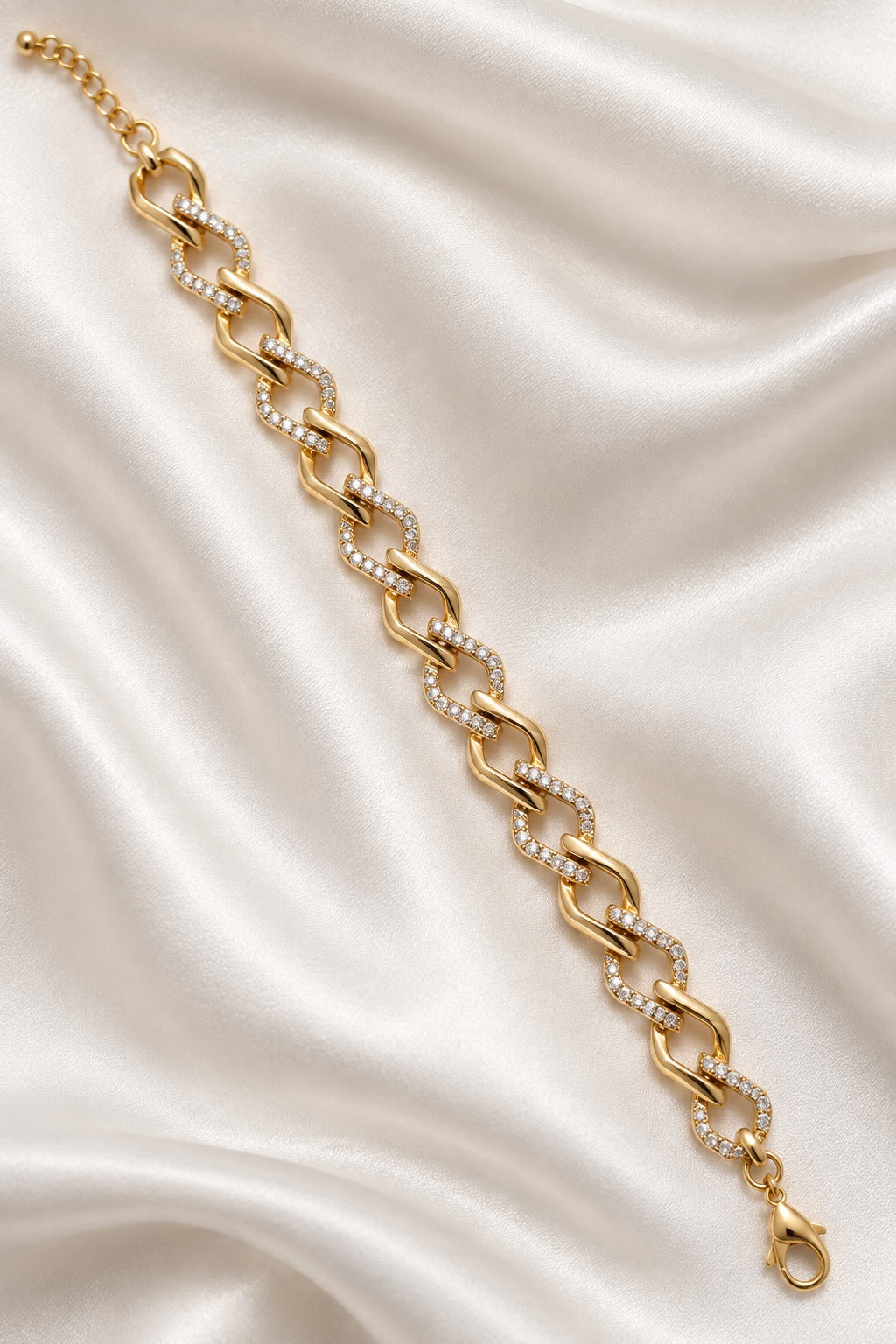 A gold chain bracelet with alternating links set with small clear stones, displayed diagonally on a draped white satin fabric background. Gilded Spark Gold Zirconia Link Bracelet | Harma Jewelry 18k gold plated