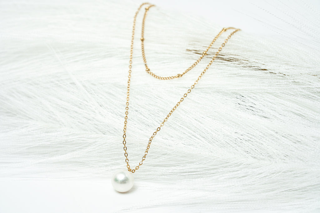 Gold necklace with a pearl pendant on a textured white surface