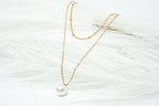 Gold necklace with a pearl pendant on a textured white surface