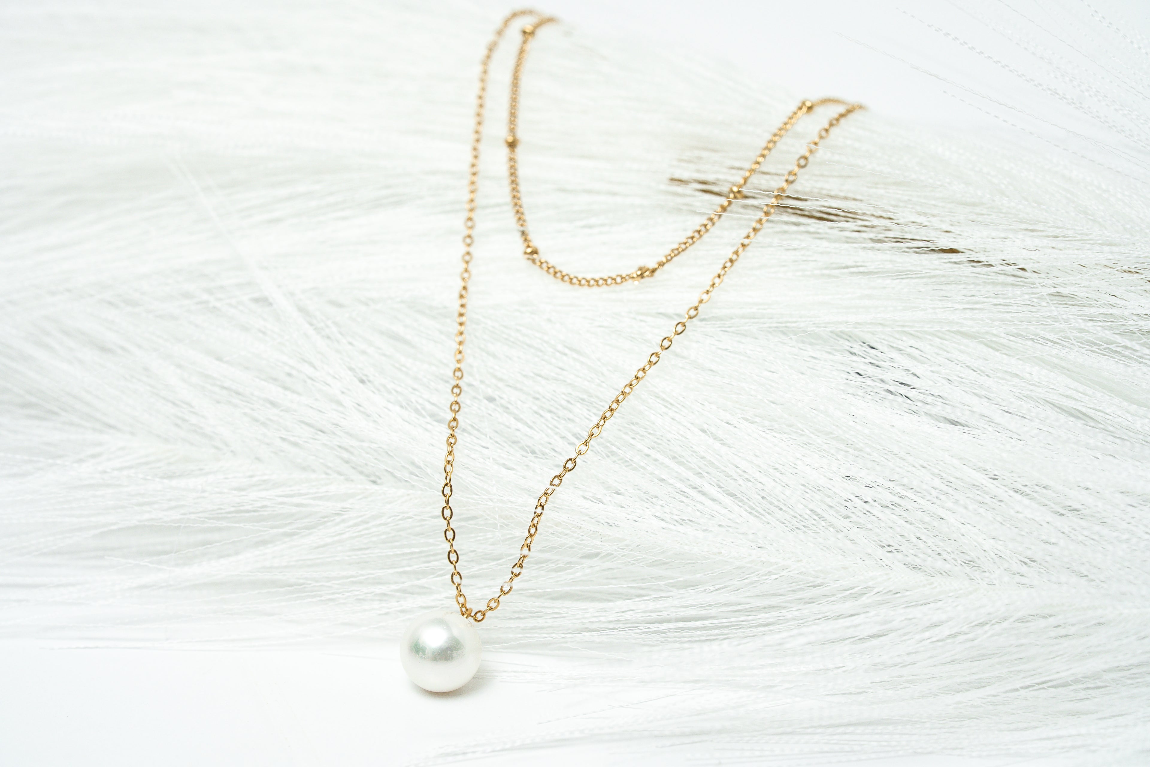 Gold necklace with a pearl pendant on a textured white surface
