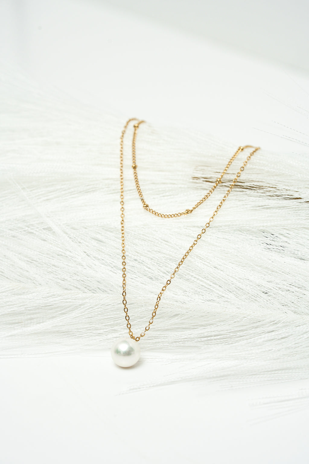 Gold necklace with a pearl pendant on a textured white surface