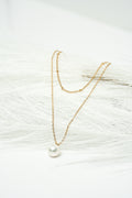 Gold necklace with a pearl pendant on a textured white surface