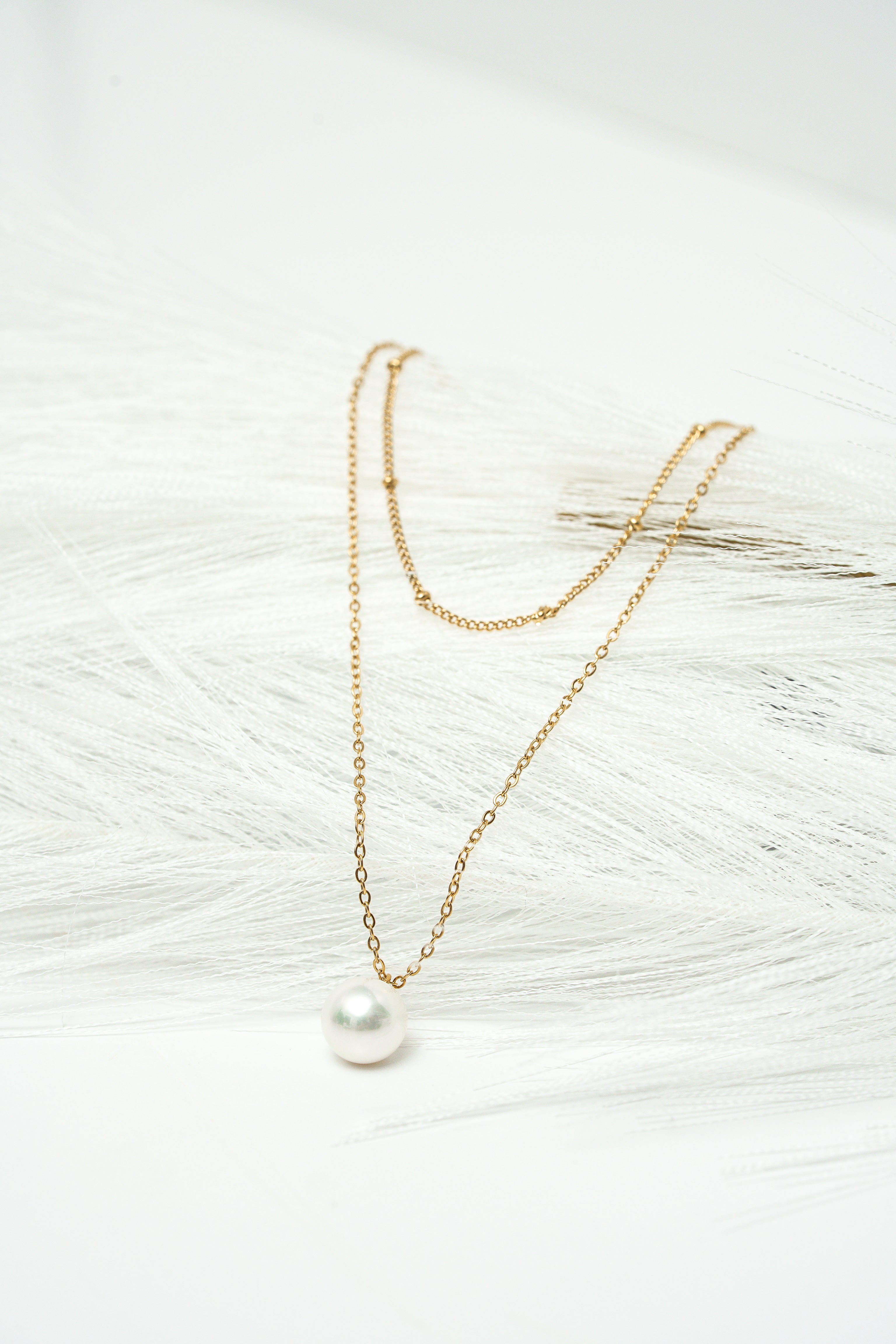 Gold necklace with a pearl pendant on a textured white surface