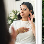 Woman adjusting earrings in front of a mirror with decorative elements.