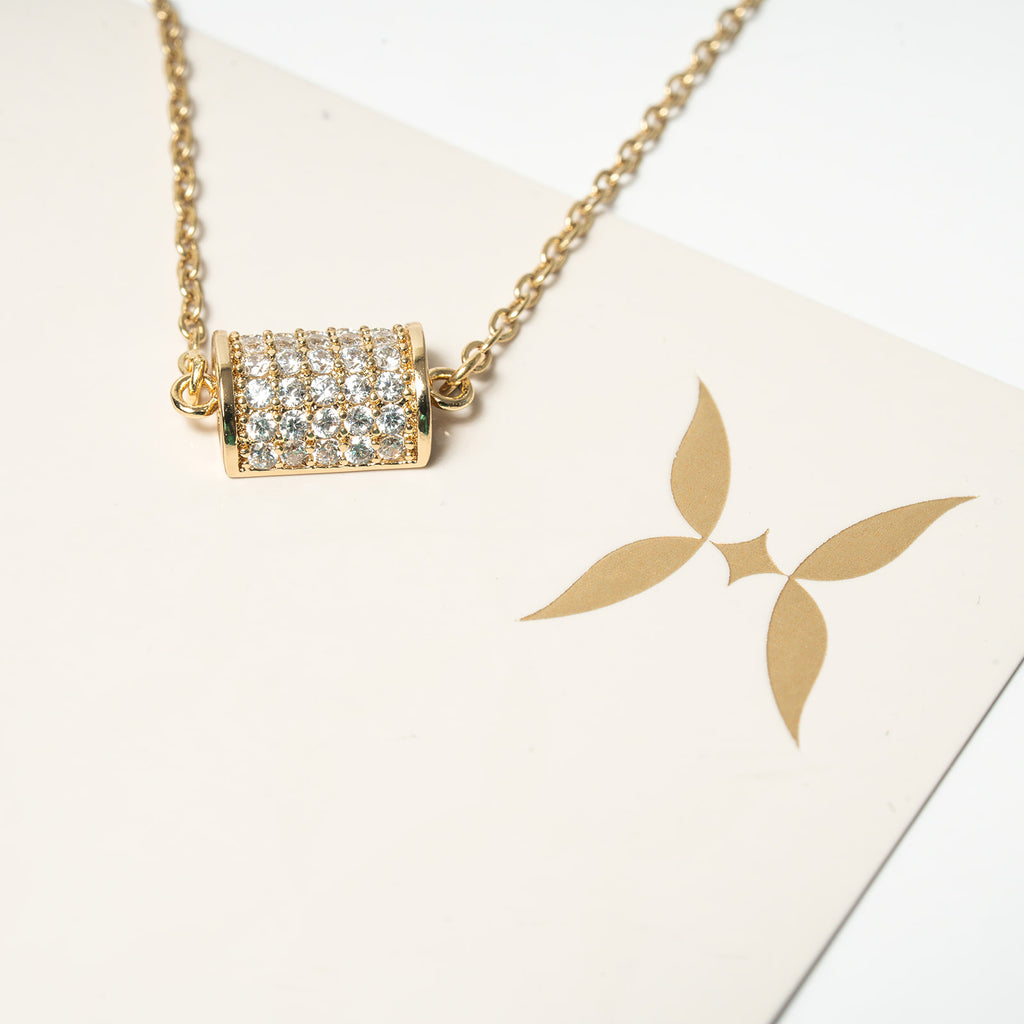 Gold necklace with a diamond pendant on a white card with a gold logo. Harma 14k gold plated Golden Barrel Chain Bracelet