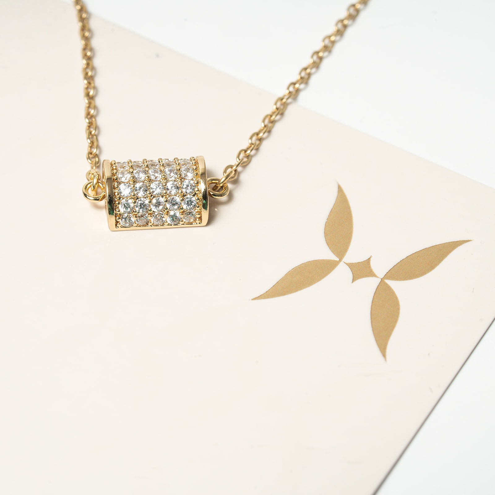 Gold necklace with a diamond pendant on a white card with a gold logo. Harma 14k gold plated Golden Barrel Chain Bracelet