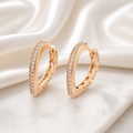 Rose gold hoop earrings with diamond accents on a soft white fabric background