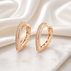 Rose gold hoop earrings with diamond accents on a soft white fabric background
