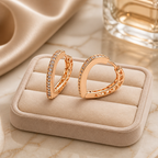 Rose gold hoop earrings with embedded stones on a beige jewelry cushion.