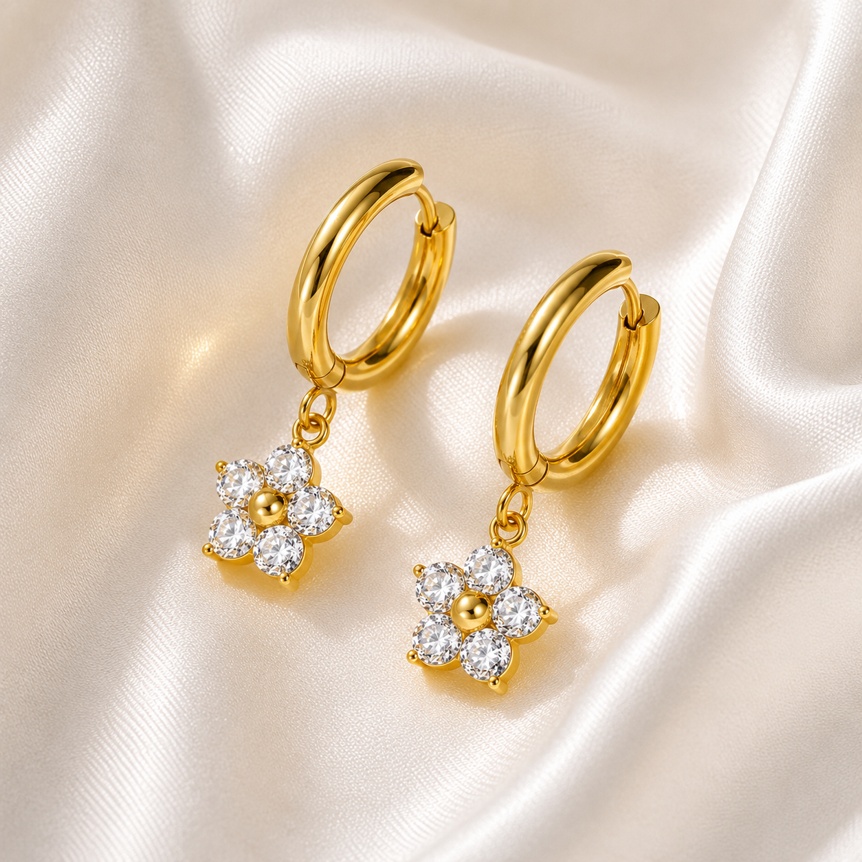 Gold hoop earrings with floral charms on a satin background