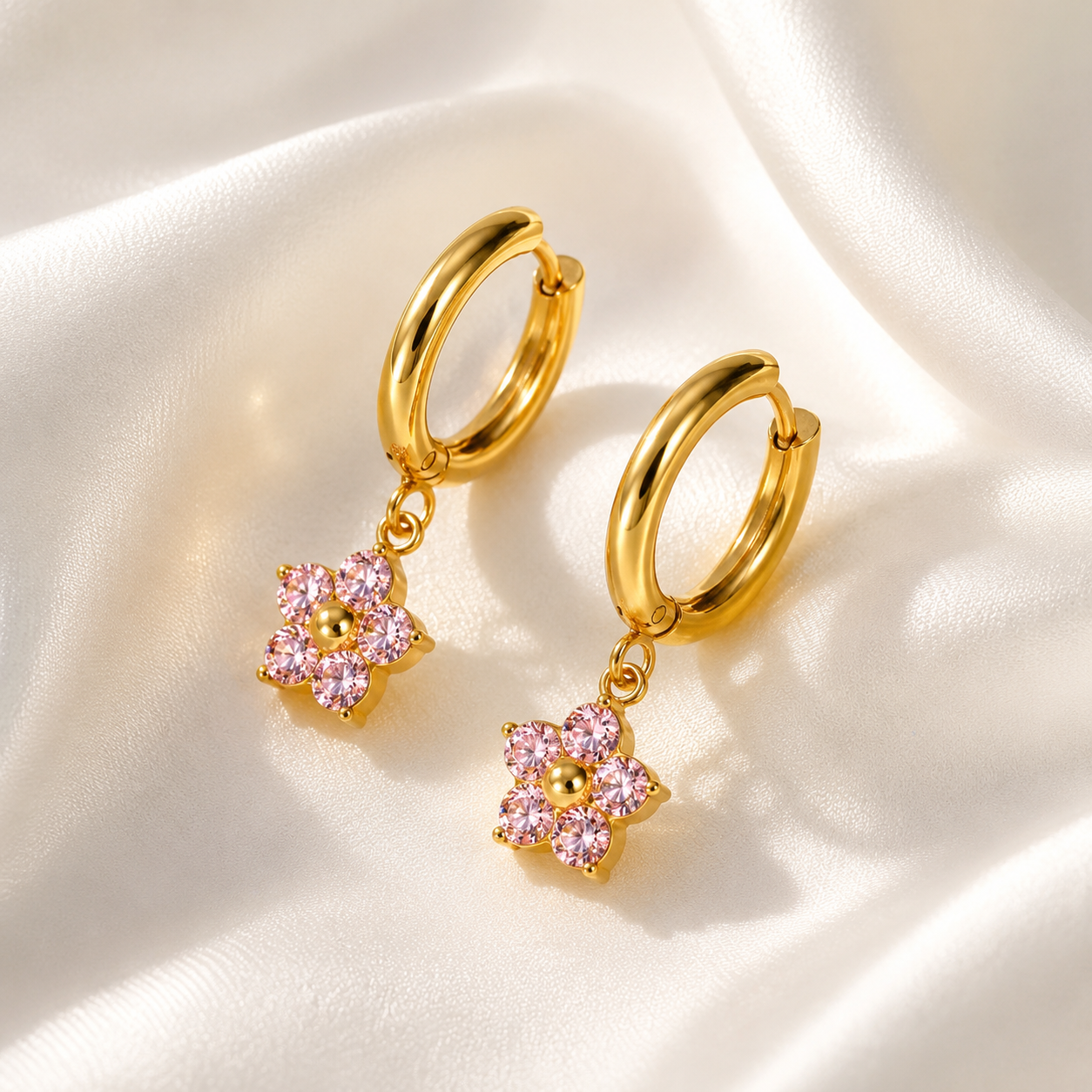 Gold hoop earrings with pink flower charms on a white fabric background