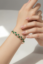 Hand wearing a green gemstone bracelet on a neutral background