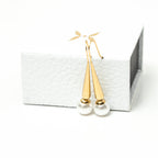 Gold earrings on a white card with a white background. Harma Gold Plated Pearl I Am Grounded Dangle Earrings