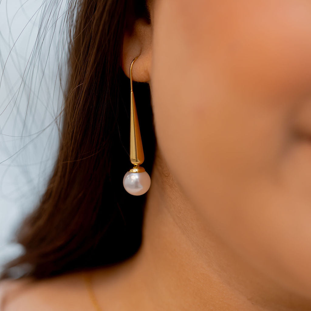 Close-up of a person wearing gold earrings and a necklace with a blurred background. Harma Gold Plated Pearl I Am Grounded Dangle Earrings