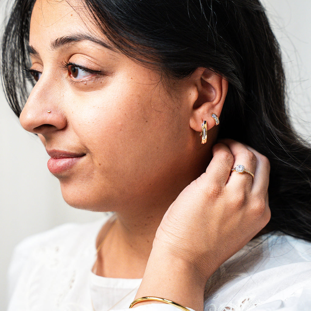 Woman adjusting an earring with a plain background. Harma Gold Plated Resilient Spark Gold Earrings