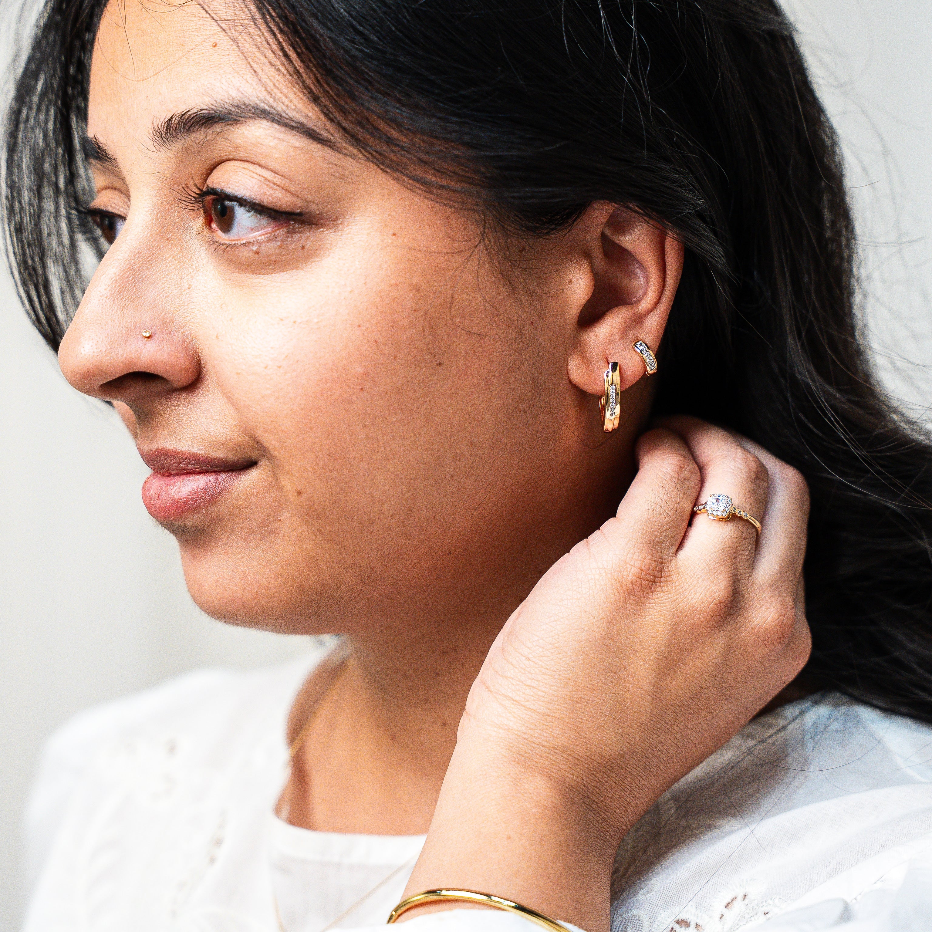 Woman adjusting an earring with a plain background. Harma Gold Plated Resilient Spark Gold Earrings