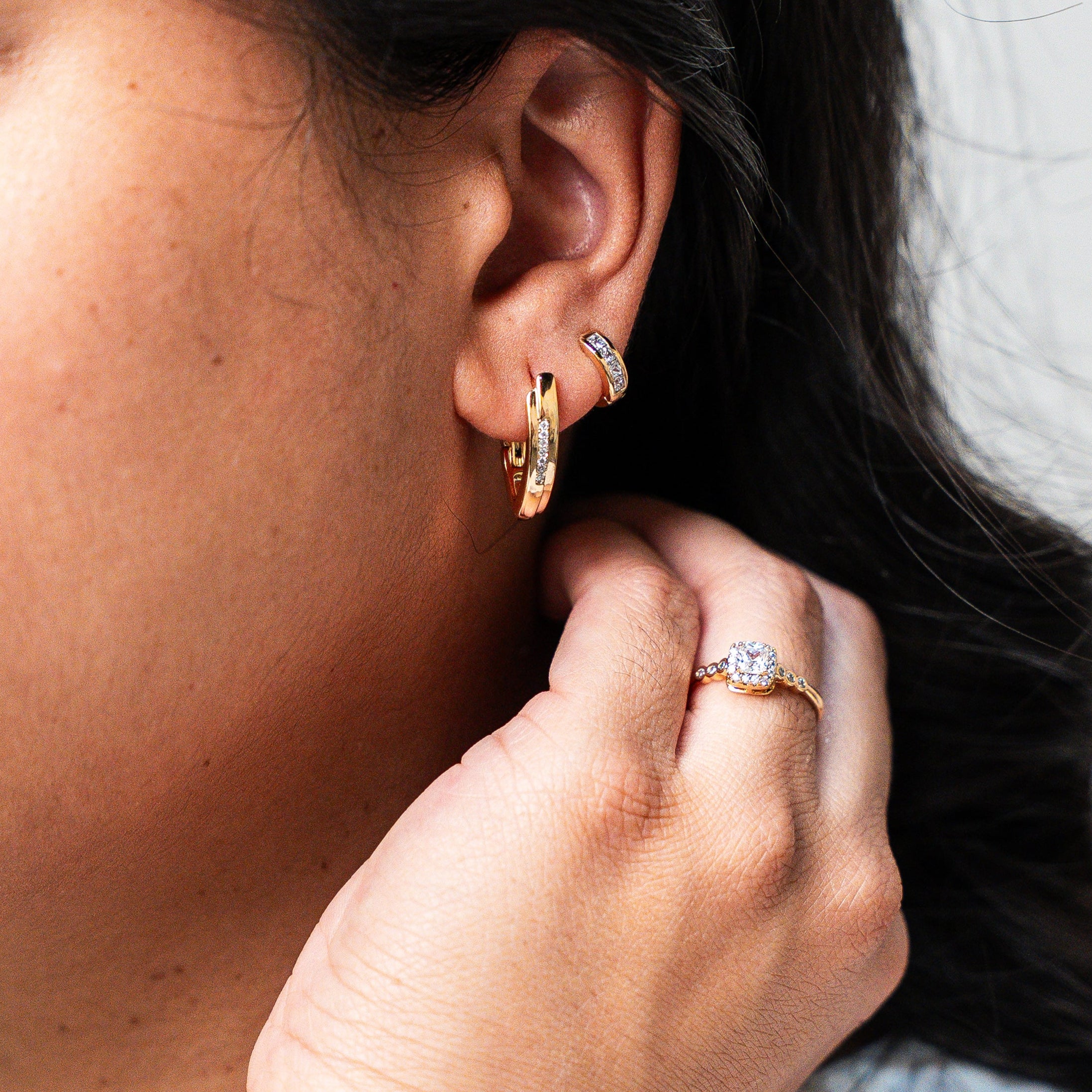 Close-up of a person wearing earrings and a ring, with a neutral background. Harma Gold Plated Resilient Spark Gold Earrings