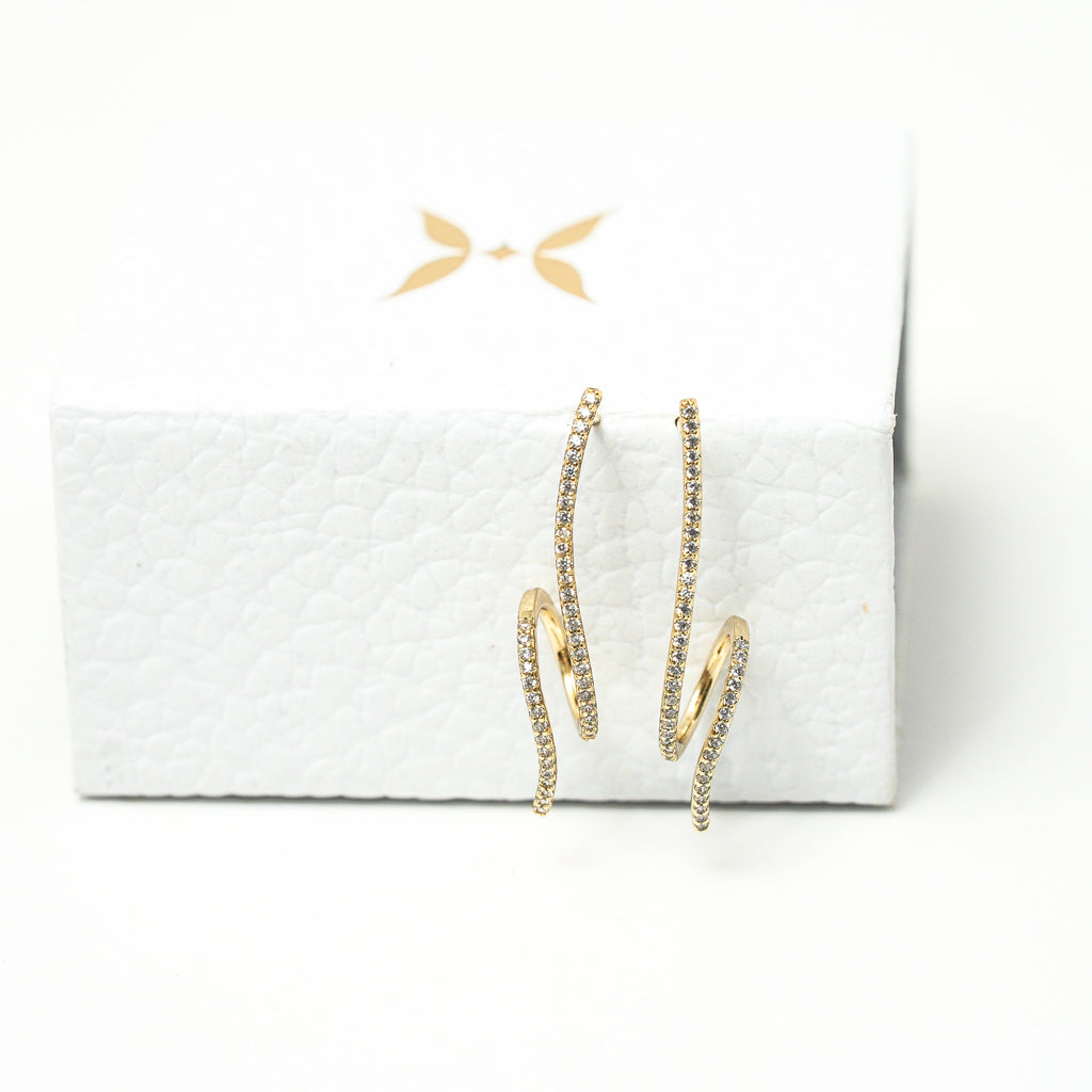 Gold hoop earrings on a white box with a white background. Harma Gold plated Rise in Flow Sparkle Earrings