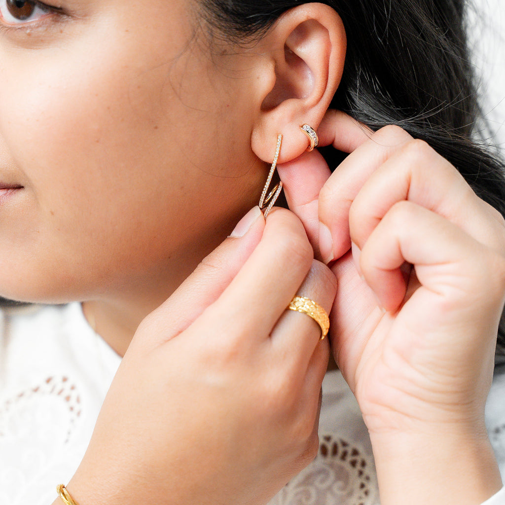 Person wearing a gold earring and adjusting it with their hand. Harma Gold plated Rise in Flow Sparkle Earrings