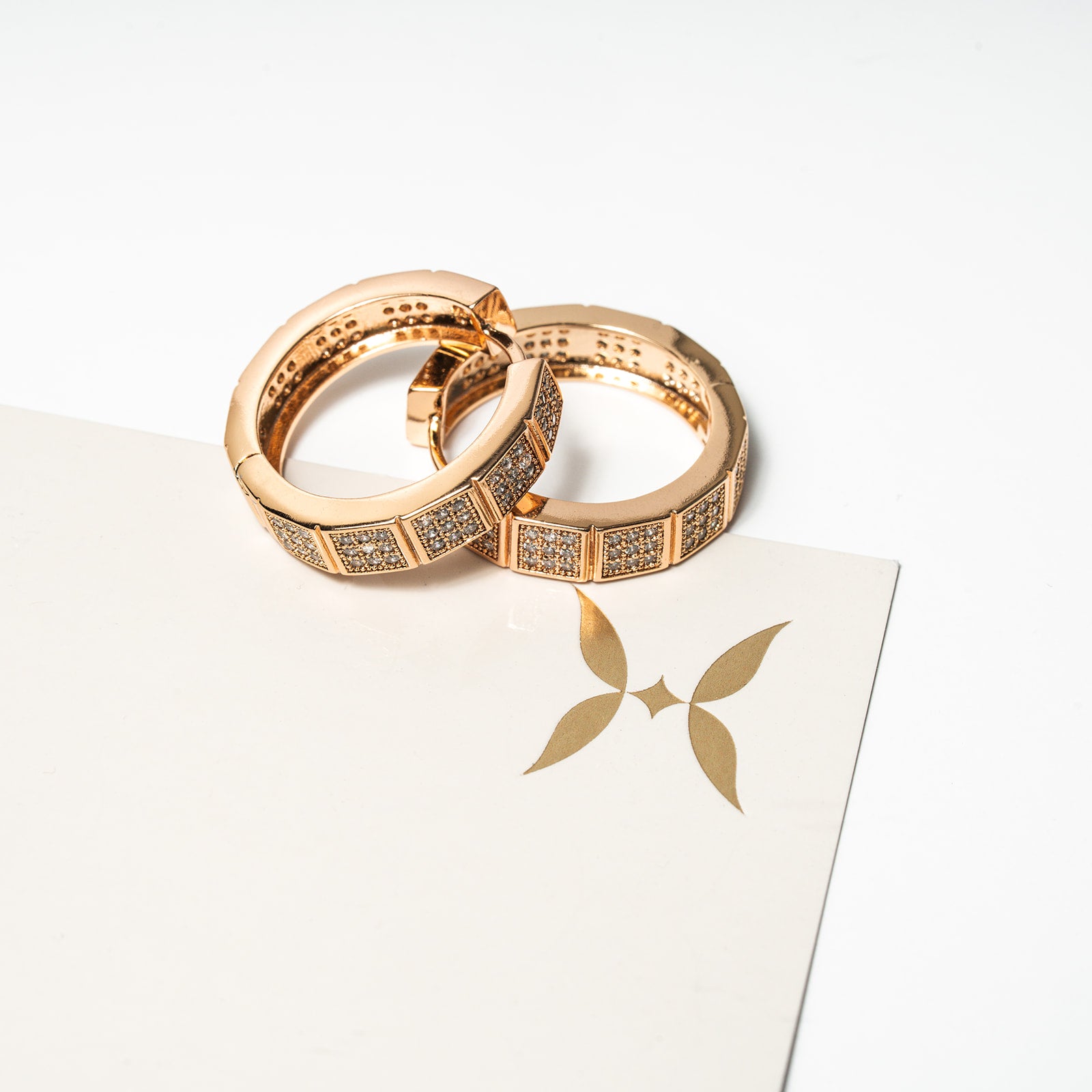 Two rose gold rings on a white card with a logo Harma Horizon Edge Zirconia Hoop Earrings