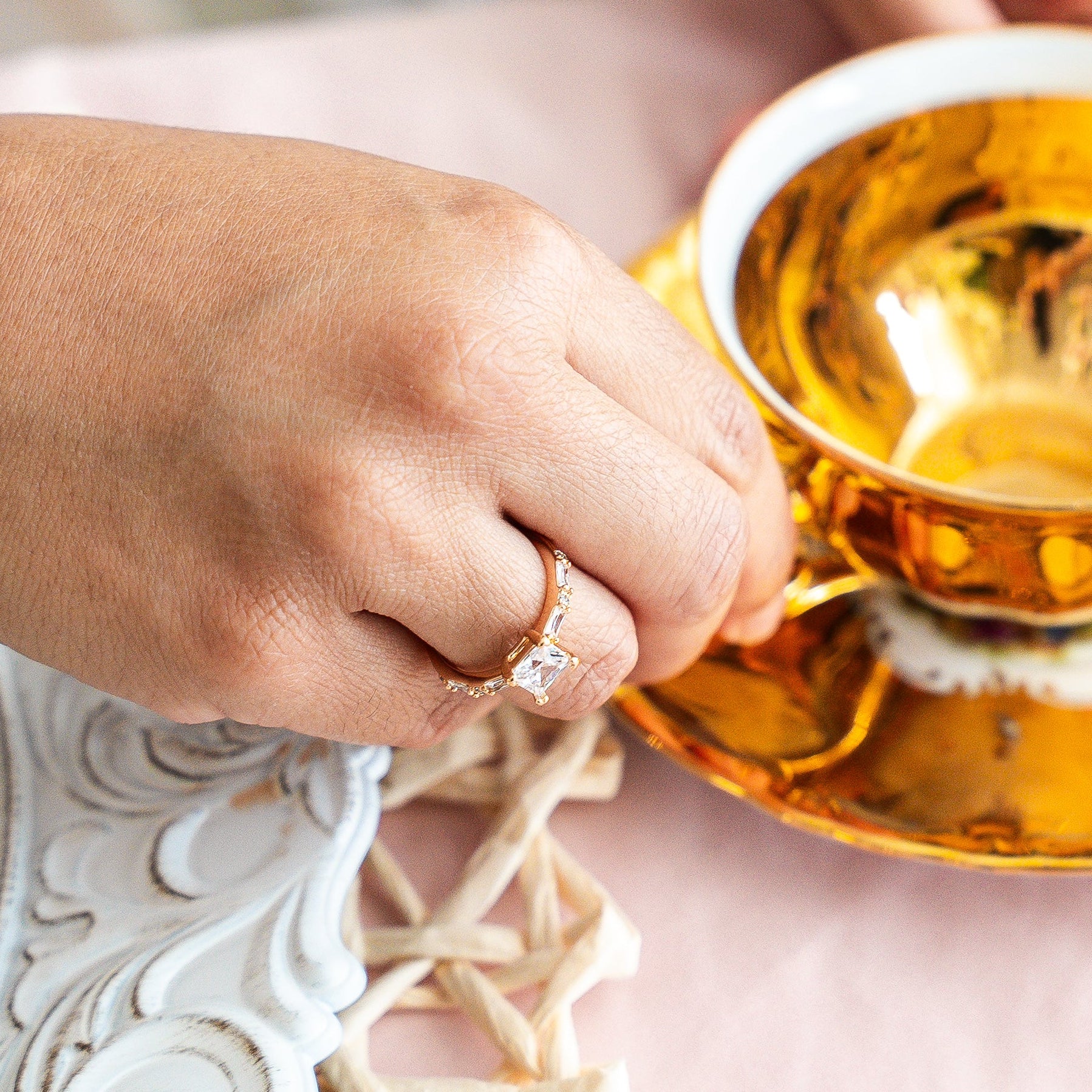 Two people holding gold teacups with saucers on a decorative table.