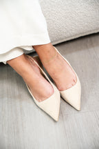 Beige pointed-toe shoes worn indoors on a light wooden floor.