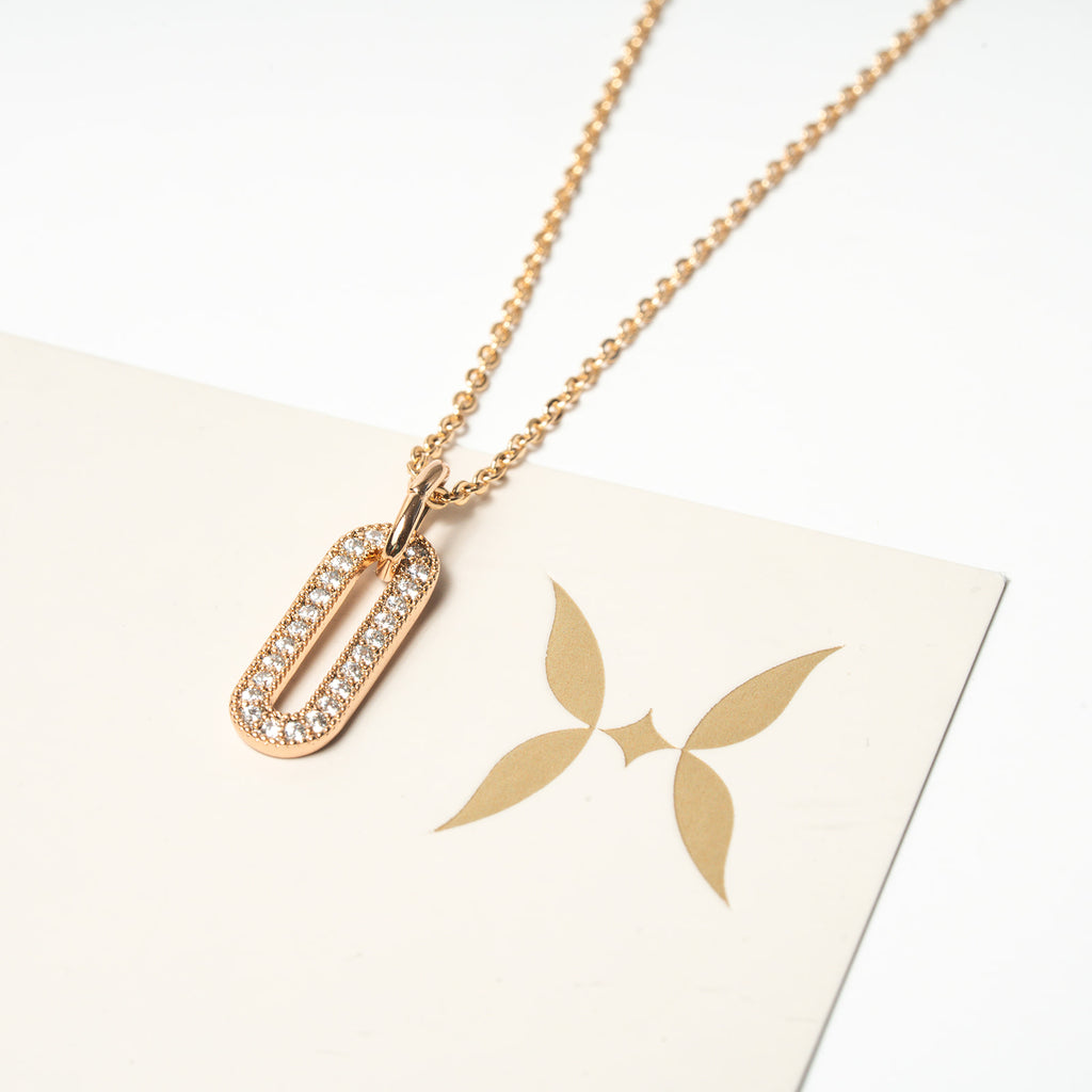 Gold necklace with a pendant on a white surface. Harma Jewelry Cubic Zirconia Incrusted Sumptuous Paper Clip Pendant Necklace Set