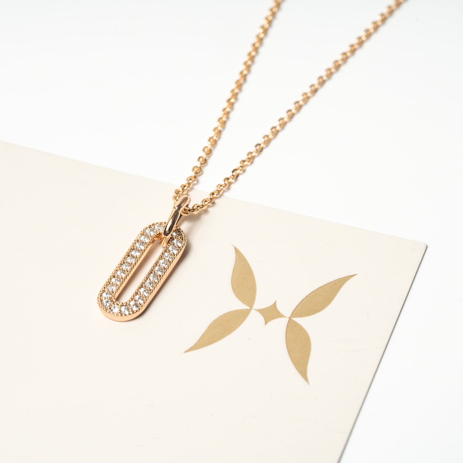 Gold necklace with a pendant on a white surface. Harma Jewelry Cubic Zirconia Incrusted Sumptuous Paper Clip Pendant Necklace Set