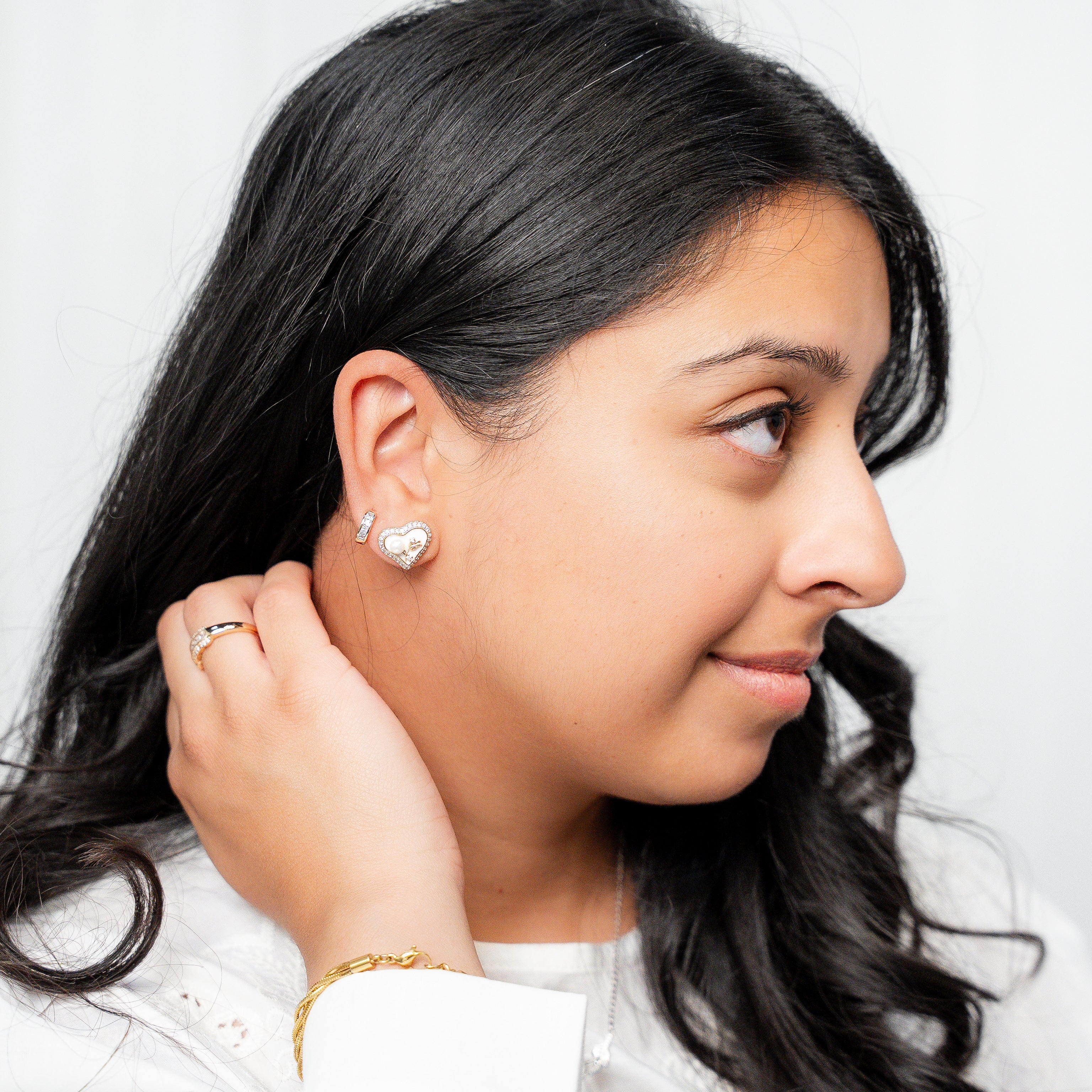 Woman adjusting an earring against a plain background